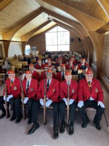Veteran Honor Guard and bagpipe band members sitting indoors at a veteran memorial