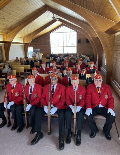 Veteran Honor Guard and bagpipe band members sitting indoors at a veteran memorial
